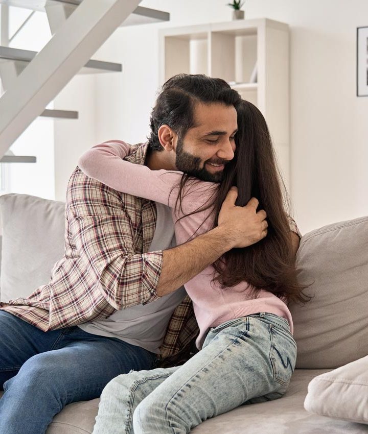 a father hugs her daughter happily while they are sitting on the couch