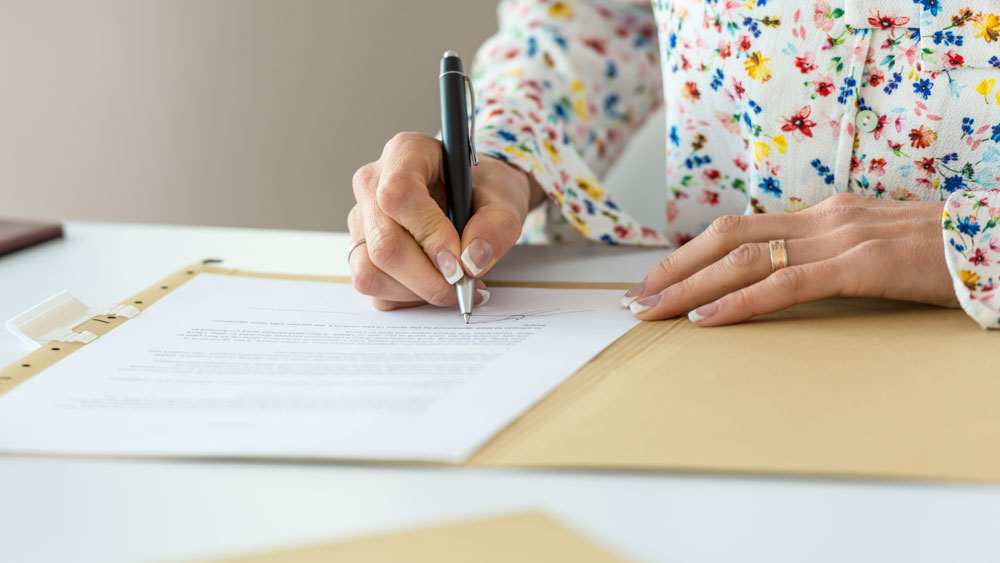 Closeup of a woman signing an agreement or contract in a folder