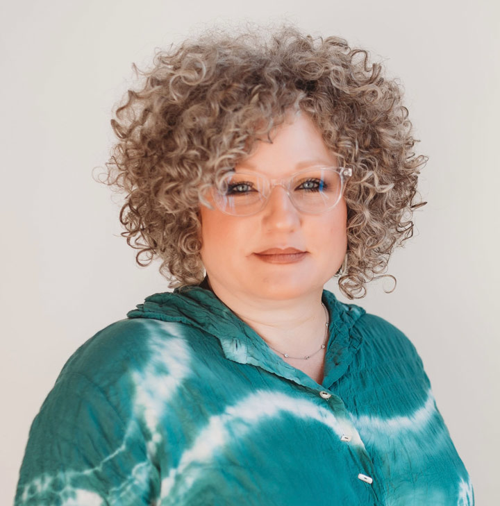photo of a lady wearing transparent framed glasses, green and white blouse and a beautiful curly hair