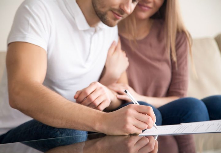 Close up of couple signing documents, young man putting signature on document, his wife sitting next to husband holding his arm, real estate purchase, first time home buyers, prenuptial agreement